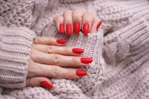 De las mujeres manos con un hermosa mate oval manicura en un calentar rosado de punto suéter. invierno tendencia, cubrir rojo uñas con gel polaco, goma laca. foto