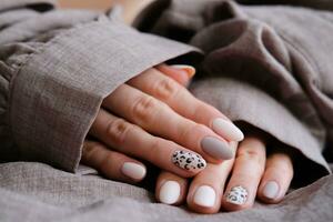 A woman's hand with a beautiful manicure holds a beige fabric. Autumn trend, beige color polishing with leopard pattern on nails with gel polish, shellac. photo