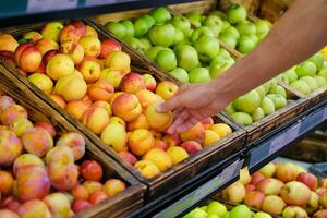 A man's hand chooses a nectarine on a store counter. A man buys a peach at the market. Fruits, healthy food. photo