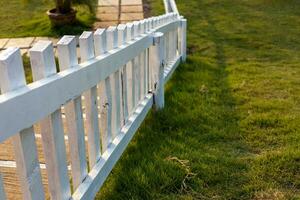 Close-up view of a white wooden fence installed against the sunlight on the lawn. photo