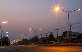 Scenery of orange starbursts from street lamp posts illuminating the road near residential houses. photo