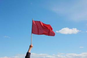 Hand holding red flag against blue sky photo