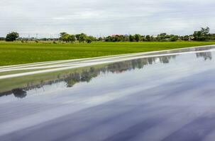 A close-up view of a reflection on a blue solar panel over green rice paddies. photo