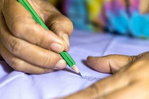 Close-up low view of elderly female hand holding a pencil to write letters on a white. photo