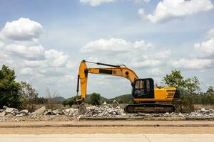 A view of a yellow backhoe parked on the pavement of a demolished concrete road. photo