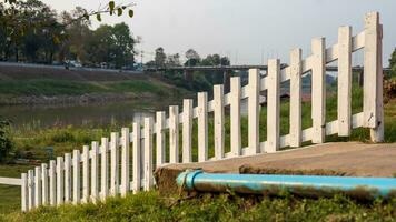 A close-up view of a white wooden fence stretched across the lawn near a concrete platform. photo