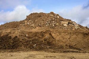 Excavated mounds of sand and concrete rubble are piled together against wheel traces. photo