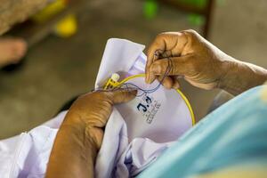 Close-up view of an elderly woman hand using a needle and blue thread to embroider. photo