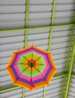 A low-angle view passes through a colorfully decorated umbrella hanging beneath a roof structure. photo