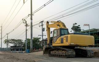 View of an old yellow backhoe parked on the road being renovated. photo