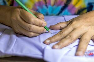 Close-up low view of elderly female hand holding a pencil to write letters on a white. photo