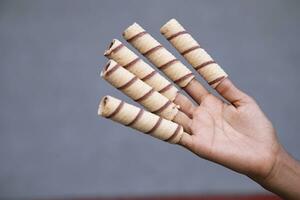 Hand-holding wafer rolls with chocolate on gray background, close up photo