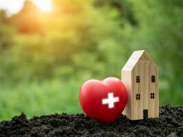 The concept of health insurance and medical welfare. Model wooden house and red heart with plus icon. Health insurance and access to health care. health care planning photo