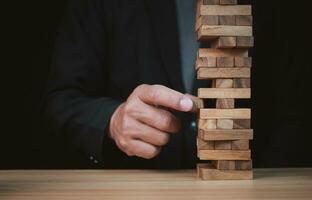 Businessman hand of businessman pulling out or placing wood block on the tower with copyspace. Business risk, strategy and planing concept idea. photo