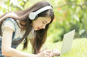 Asian woman working with laptop and smiling happily in park photo