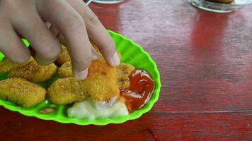 the hand of a woman who is taking chicken nuggets and smeared with sauce video