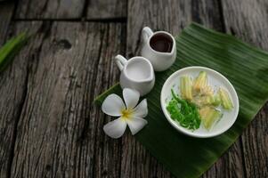 Lod Chong fragrant pandan rice dripping into coconut milk in a wooden bowl on a green banana leaf background. or Lod Chong mixed with Thai melons Asian Thai desserts photo