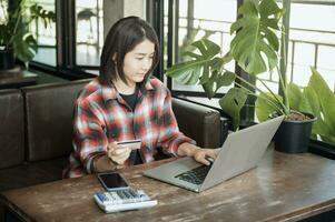 asiático mujer participación el plastico crédito tarjeta y utilizando ordenador portátil en línea compras concepto. tono imagen. foto