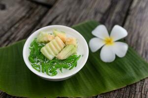 Lod Chong fragrant pandan rice dripping into coconut milk in a wooden bowl on a green banana leaf background. or Lod Chong mixed with Thai melons Asian Thai desserts photo