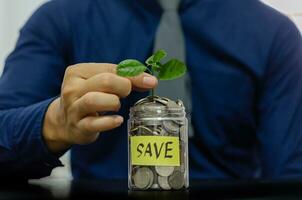 un hombre participación un tarro con monedas y un planta foto