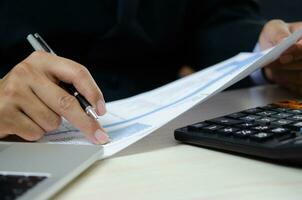 Businessperson reviewing documents with pen, analyzing data on graph report statistic and chart finance, budget, investment, accountant, diagram on desk. photo