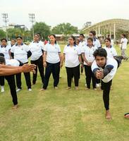 New Delhi, India, June 21, 2023 - Group Yoga exercise session for people at Yamuna Sports Complex in Delhi on International Yoga Day, Big group of adults attending yoga class in cricket stadium photo