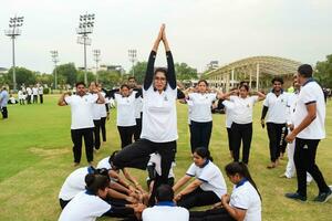 New Delhi, India, June 21, 2023 - Group Yoga exercise session for people at Yamuna Sports Complex in Delhi on International Yoga Day, Big group of adults attending yoga class in cricket stadium photo