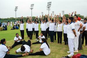 New Delhi, India, June 21, 2023 - Group Yoga exercise session for people at Yamuna Sports Complex in Delhi on International Yoga Day, Big group of adults attending yoga class in cricket stadium photo