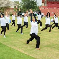 New Delhi, India, June 21, 2023 - Group Yoga exercise session for people at Yamuna Sports Complex in Delhi on International Yoga Day, Big group of adults attending yoga class in cricket stadium photo