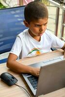 Little boy sitting at table using laptop for online class in Grade 1, Child studying on laptop from home for distance learning online education, School boy children lifestyle concept photo