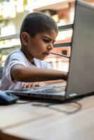 Little boy sitting at table using laptop for online class in Grade 1, Child studying on laptop from home for distance learning online education, School boy children lifestyle concept photo