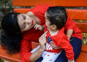 amoroso mamá que lleva de su bebé a sociedad parque. brillante retrato de contento mamá participación niño en su manos. madre abrazando su pequeño 9 9 meses antiguo hijo. foto