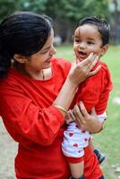 Loving mom carrying of her baby at society park. Bright portrait of happy mum holding child in her hands. Mother hugging her little 9 months old son. photo