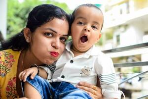 Loving mom carrying of her baby at home balcony. Bright portrait of happy mum holding child in her hands. Mother with her little 1 year old son. photo