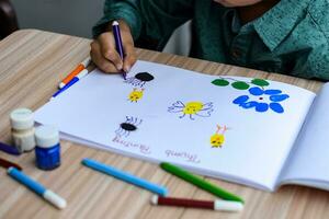 Smart Indian little boy perform thumb painting with different colourful water colour kit during the summer vacations, Cute Indian Kid doing colourful thumb painting drawing on wooden table photo