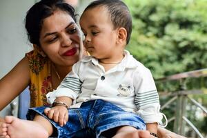 Loving mom carrying of her baby at home balcony. Bright portrait of happy mum holding child in her hands. Mother with her little 1 year old son. photo