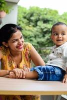 Loving mom carrying of her baby at home balcony. Bright portrait of happy mum holding child in her hands. Mother with her little 1 year old son. photo