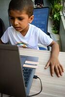 Little boy sitting at table using laptop for online class in Grade 1, Child studying on laptop from home for distance learning online education, School boy children lifestyle concept photo