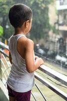 Little kid playing in summer rain in house balcony, Indian smart boy playing with rain drops during monsoon rainy season, kid playing in rain photo