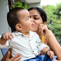 Loving mom carrying of her baby at home balcony. Bright portrait of happy mum holding child in her hands. Mother with her little 1 year old son. photo