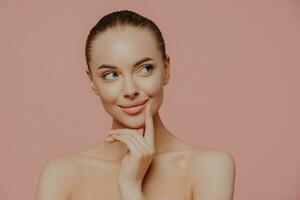 Thoughtful topless lady with perfect skin, undergoing facial treatments, isolated indoors. Cosmetology and wellness concept. photo