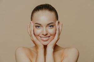 alegre mujer con Perfecto sonrisa, toques cara suavemente. limpio, sano piel. piel cuidado y belleza concepto. foto