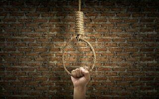 Hand holding rope noose with hangman's knot hanging on dark brick wall photo
