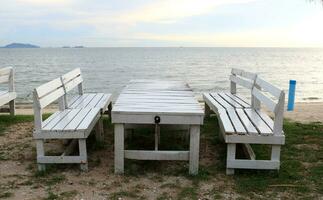 Set white painted table and benches on sand and sea, sky background with sunlight, white cloud in sky. photo