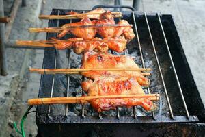 Chicken in bamboo clamp roasting on retro charcoal stove, street food in Thailand. photo
