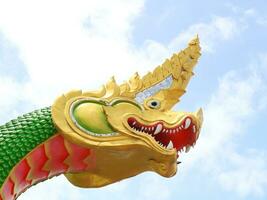 Green serpent cement statue, head gold color head and white cloud in blue sky background. photo