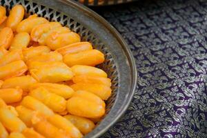 Med Khanoon Thai dessert made from mung bean paste in oval shape and coating by yolk egg on plate above Thai ancient pattern cloth. photo