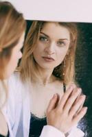 Beautiful caucasian blonde young woman in white shirt standing by the mirror. Health care, beauty, mental issues photo