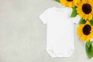 White baby girl or boy bodysuit mockup flat lay with sunflowers on gray concrete background. Design onesie template, print presentation mock up. Top view. photo