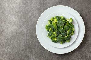 Raw broccoli on a white plate on a dark gray concrete background. Top view. Copy space. photo